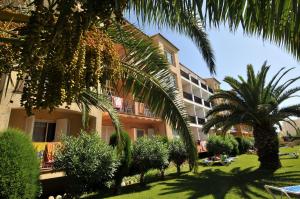 a building with palm trees in front of a yard at Bertur Gran Reserva Comte Empuries in Empuriabrava