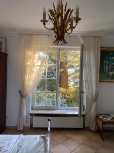 ein Schlafzimmer mit einem Fenster mit Vorhängen und einem Kronleuchter in der Unterkunft Inge's Arthouse & Gardenlounge, bei Frankfurt in Eschborn