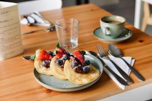a plate of pancakes with strawberries and blueberries and a cup of coffee at Palermo Inn Boutique Arte in Palermo