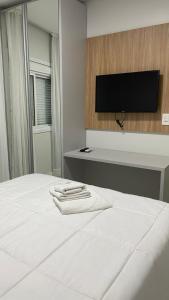 um quarto com uma cama branca e uma televisão de ecrã plano em Pousada Onix em Ametista do Sul