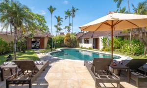 a villa with a swimming pool with chairs and an umbrella at Bali Dyana Villas in Seminyak