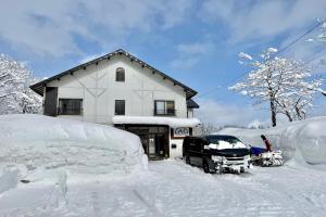 a house covered in snow with a truck in front at Myoko House in Myoko