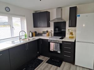 a kitchen with black cabinets and a white refrigerator at Large Swindon House Big Garden for Photoshoot in Swindon