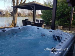 a jacuzzi tub in a yard with an umbrella at Elite Retreats 4U Lakeside Hot Tub Log Cabin at Tattershall Lakes Park in Tattershall