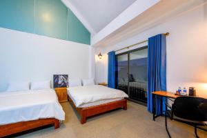 Un dormitorio con dos camas y un escritorio y una ventana. en Orchid Villa, en Kỳ Vĩ