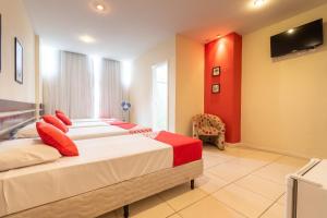 two beds in a bedroom with a red wall at OYO Hotel L'Espace - Jaraguá Belo Horizonte in Belo Horizonte