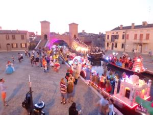 Un grupo de personas de pie alrededor de un río con barcos. en Primavera 2-1, en Lido di Pomposa