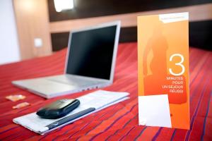 a table with a laptop and a cell phone and a book at CLASSIC HÔTEL Reims Est - Taissy in Reims