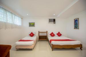 two beds in a room with white walls and red pillows at OYO 588 Sunrock Resort in Antipolo