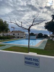 Un cartel frente a una piscina con un árbol en Las fuentes, en Alcossebre