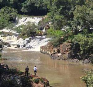 two people walking in a river with a waterfall at Joa y Santi in Jardín América