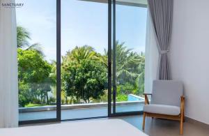 a bedroom with a bed and a chair and a large window at Villa Hồ Tràm 4 Phòng Hồ bơi riêng cao cấp - Sanctuary Resort in Ho Tram
