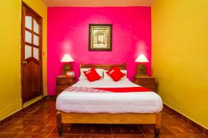 a bedroom with a pink wall and a bed with red pillows at OYO Posada De Los Angeles, Pátzcuaro in Pátzcuaro