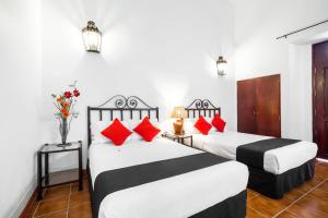 two beds in a hotel room with red pillows at Capital O El Nito Posada in Oaxaca City