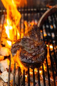 a piece of meat cooking on a grill with flames at Bella Vista Hôtel, Suites & Maisons in Porticcio