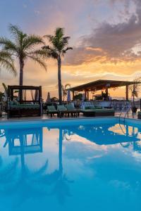 a swimming pool with palm trees and a sunset at Bella Vista Hôtel, Suites & Maisons in Porticcio