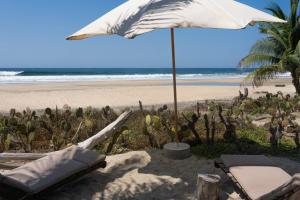 a beach with chairs and an umbrella on the beach at Cabanas Adobe Frente Al Mar in Puerto Escondido +119 photos