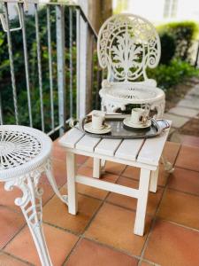 zwei weiße Stühle und ein Tisch mit Tassen und Untertassen in der Unterkunft Inge's Arthouse & Gardenlounge, bei Frankfurt in Eschborn