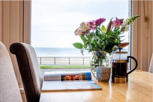 a table with a vase of flowers and a book at St Kitts Apartment in Filey