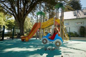 a little girl is riding on a toy car on a playground at Camping Au Soir D'été in Mesquer