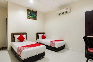 two beds in a room with white walls and red pillows at Super OYO 89427 Kavanas Hotel Taiping in Taiping