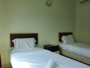 two beds in a hotel room with white sheets at Hotel O Good View Inn in Sri Aman