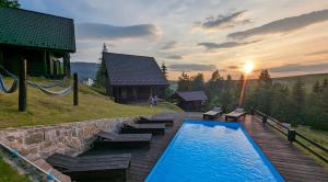 a swimming pool with benches and a house with the sunset at Cottages Shepit Lisu in Rosokhach