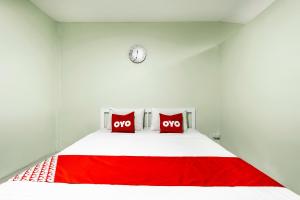 a bed with two red pillows and a clock on the wall at I Oun Inn in Nakhon Nayok