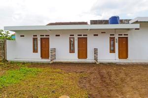 une maison blanche avec des portes brunes et une cour dans l'établissement OYO 90809 Homestay Black Pink Merah Jambu Syariah, à Garut