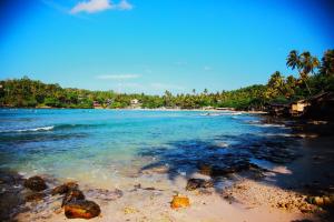 a beach with rocks and the ocean and palm trees at Dilmalee Village in Dickwella