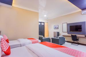 a room with two beds and a desk and a tv at Hotel O Wisma Kuta Karang in Lhokseumawe