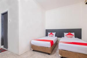two beds in a room with white walls and red pillows at Hotel O Transit 2 in Makassar