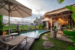 una piscina all'aperto con sedie e ombrellone di The Macaw Ubud Green Uma Villa a Blahbatu