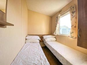 Dos camas en una habitación pequeña con ventana. en Homely 8 Berth Caravan With Side Decking And Ramp Access In Kent, Ref 47018H, en Whitstable