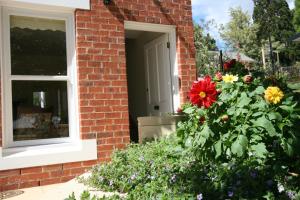 a brick house with a window and a bush of flowers at Annies Garden Cottage in Hobart