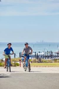 dwoje ludzi jeżdżących rowerami po drodze blisko oceanu w obiekcie Stay Rottnest w mieście Wyspa Rottnest