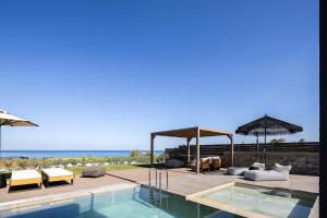 a swimming pool with chairs and umbrellas next to the ocean at Villa Aya - Coastal Villa, Minimalist Elegance by etouri in Stavromenos