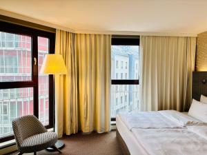 a hotel room with a bed and a chair and windows at Max Brown Hotel 5th District, part of Sircle Collection in Vienna