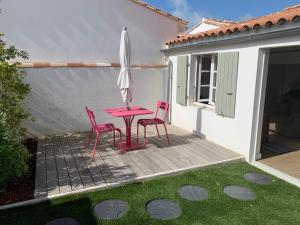 a patio with a pink table and chairs and an umbrella at Hotel Les Bois Flottais in Le Bois-Plage-en-Ré