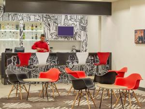 a bar with red chairs and a woman in the background at ibis Ankara Airport Hotel in Ankara