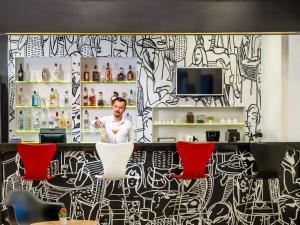 a man standing behind a bar with red chairs at ibis Ankara Airport Hotel in Ankara
