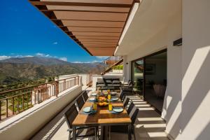 a balcony with wooden tables and chairs and mountains at Modern penthouse with two terraces, jacuzzi and sea, lake and mountain views, in Almazara Hills in Istán