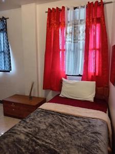 a bedroom with red curtains and a bed with a pillow at Barnwood Homestay in Talap