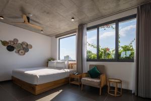 a bedroom with a bed and a chair and windows at Leaf Beachfront Hotel Da Nang in Danang