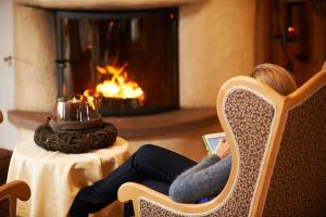 a woman sitting in a chair reading a book in front of a fireplace at Familienhotel Maria in Obereggen