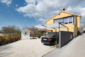 a yellow house with a car parked in a driveway at Apartment Miha in Loborika