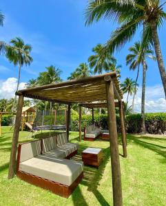 a gazebo with benches and a table and palm trees at Baía Branca Beach Resort in Tamandaré