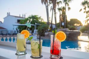 three cocktails sitting on a table next to a pool at vibes menorca in Cala en Porter