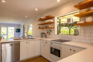 une cuisine avec des armoires blanches, un évier et une fenêtre dans l'établissement Tranquility Cottage, Oneroa - Be My Guest Waiheke, à Waiheke Island