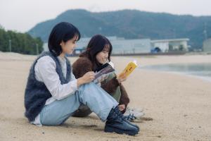 two young women sitting on the beach reading books at うみの図書館 in Sanuki